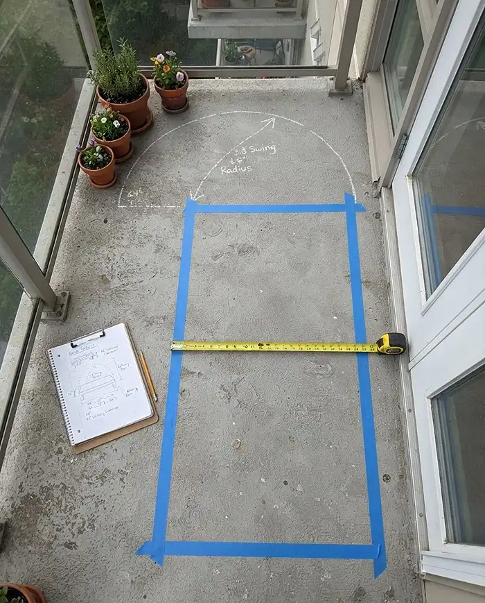 A taped bench footprint with a 24‑inch clearance and lid swing arc marked on a balcony floor, measuring for fit and traffic flow