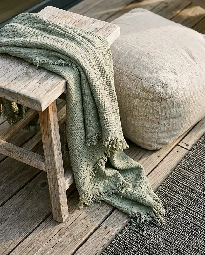 layered japandi textures with teak stool, linen cushions, and muted earth-tone textiles on a balcony